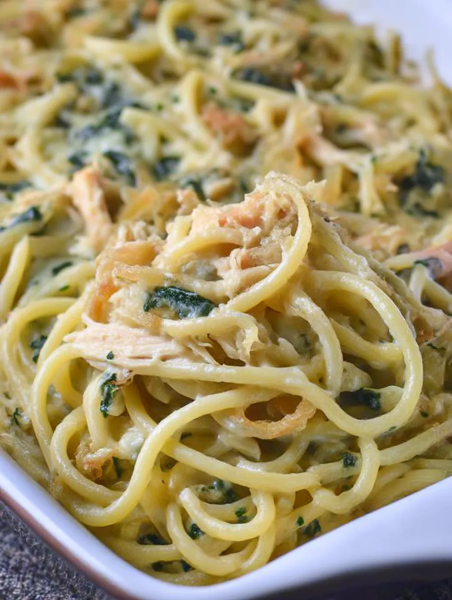 A plate with chicken spaghetti and spinach topped with crispy onions.