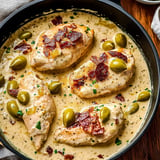 A dish of chicken with olives and herbs in a black bowl.