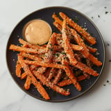 A plate of fries with a dipping sauce on a table.