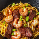 A bowl of noodles with shrimp and beef, topped with green onions.