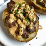 A plate of food with a potato and meat covered in sauce.