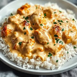 A plate of rice with a creamy sauce and chicken on top.