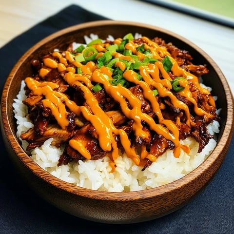 A bowl of rice with meat and sauce on top.